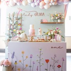 the dessert table is decorated with flowers and pastel colored balloons hanging from the ceiling