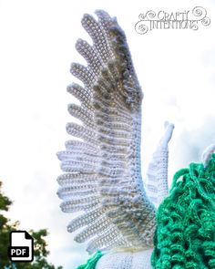 a knitted owl with wings is shown in front of the sky and has green crochet on its body