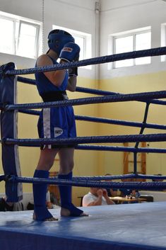 a woman standing next to a boxing ring wearing blue shorts and black gloves with her hands on the ropes