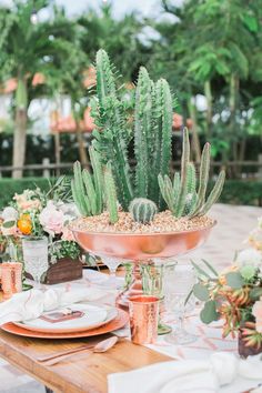 an outdoor table set with plates, glasses and succulents in copper bowls