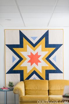 a living room with a yellow couch and a quilt on the wall above it that has a star design