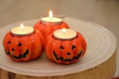 three pumpkin shaped candles sitting on top of a wooden slice