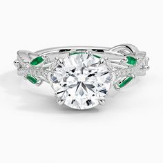 a diamond and emerald engagement ring with leaves on the band, set in 18k white gold