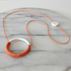 an orange and white necklace sitting on top of a marble table next to earphones