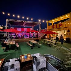 an outdoor venue with tables and benches at night, lit up by red umbrellas