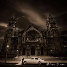 a black and white photo of a car parked in front of a church at night