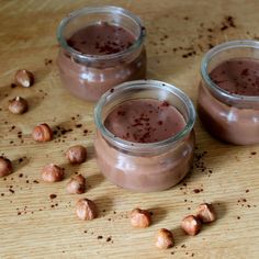 three jars filled with chocolate pudding sitting on top of a wooden table next to nuts