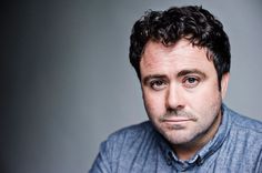 a close up of a person wearing a blue shirt and looking at the camera with a serious look on his face