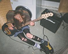 a person sitting on the ground with a guitar in their lap and headphones to their ears