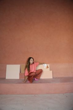 a woman sitting on top of a box in the middle of a room with pink walls