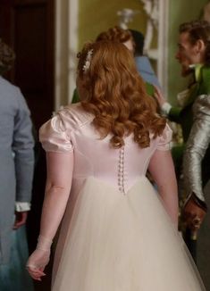 a woman with red hair wearing a white dress and pearls on her head is standing in front of other people