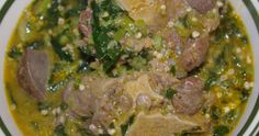 a white bowl filled with meat and vegetables on top of a green table cloth next to a wooden spoon