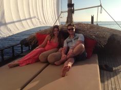 a man and woman sitting on the back of a sailboat in front of an ocean