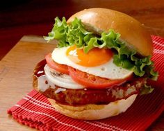 a burger with an egg, tomato and lettuce on it sitting on a red napkin