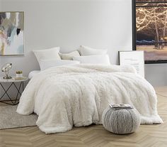 a bed with white comforter and pillows in a room next to a painting on the wall