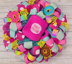 a pink and green wreath with donuts on it's side, sitting on a wooden surface