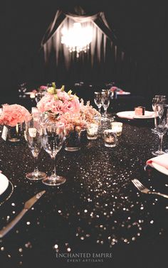 the table is set with silverware and pink flowers in vases on top of it