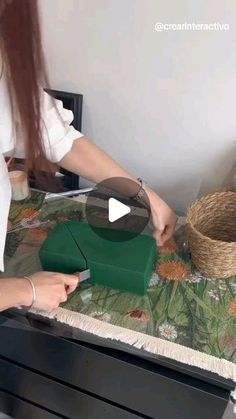 a woman is cutting paper on top of a table with a basket in front of her