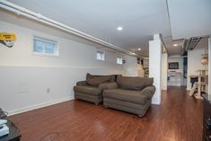 a living room with hard wood floors and white walls, two couches in the middle