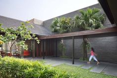 a woman walking in front of a house next to a lush green yard and trees