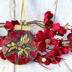 a red and gold ornament sitting on top of a wooden table next to flowers