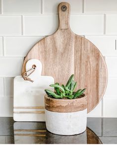 a wooden cutting board sitting on top of a table next to a potted plant