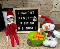 two snowmen are sitting next to a bowl of carrots and a sign that says i caught frosty picking his nose