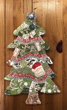 a christmas tree made out of recycled paper on a wooden surface with a santa clause ornament hanging from the top