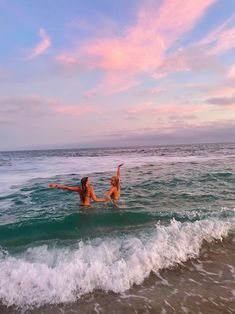 two women are playing in the water at the beach while one holds her arms up