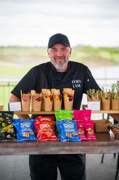 a man standing in front of a table filled with bags of chips and plants on top of it