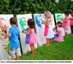 several children are painting on the side of white boards in front of a hedge wall