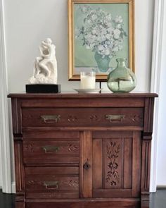 a wooden dresser with drawers and vases on top of it next to a painting