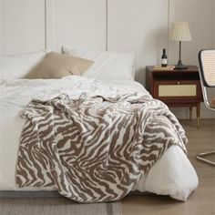 a zebra print blanket on top of a bed in a room with white walls and wooden floors