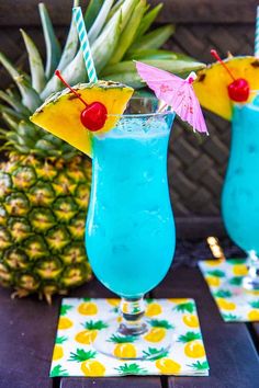 two glasses filled with blue liquid and topped with pineapples next to each other