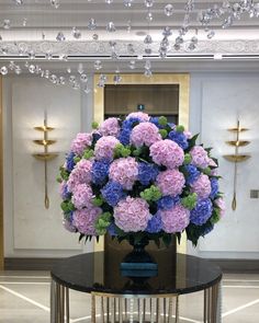 a vase filled with purple and blue flowers sitting on top of a table in front of a chandelier