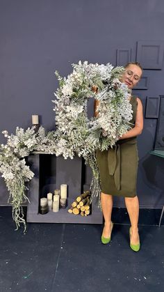 a woman is holding a wreath in front of a fireplace