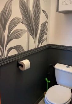 a white toilet sitting in a bathroom next to a wall with leaves painted on it