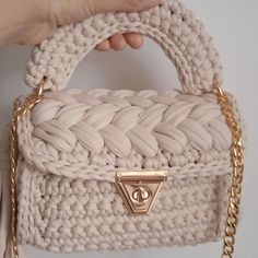 a hand holding a white purse with gold chains