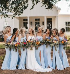 a group of women standing next to each other in front of a house with flowers