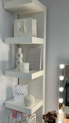 a white shelf filled with items next to a mirror and lights on top of it