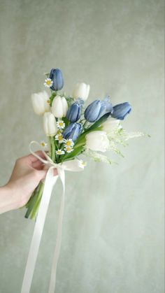 a person holding a bouquet of flowers with white and blue flowers on it's stems