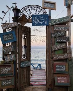 an open wooden door leading to the ocean with arabic writing on it and hanging signs