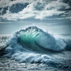 an ocean wave is breaking on the shore under a cloudy blue sky with white clouds