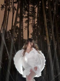 a woman is standing in the woods with her arms spread out and she's holding an umbrella over her head