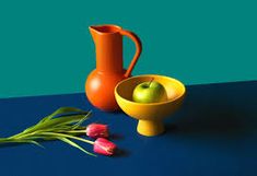 an orange pitcher and yellow bowl sit on a blue surface next to tulips