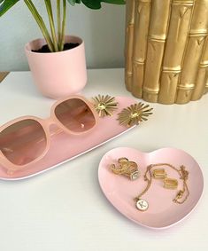 two pink heart shaped trays with sunglasses on them next to a potted plant