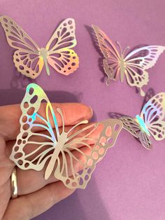 a hand is holding three paper butterflies on a purple surface, one has blue and white wings