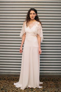 a woman standing in front of a wall wearing a white dress