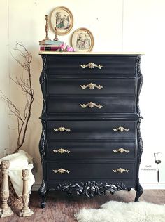 a black dresser with gold handles in a white room next to a tree and rug