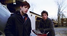 two young men standing next to each other near a car with a shopping basket in it